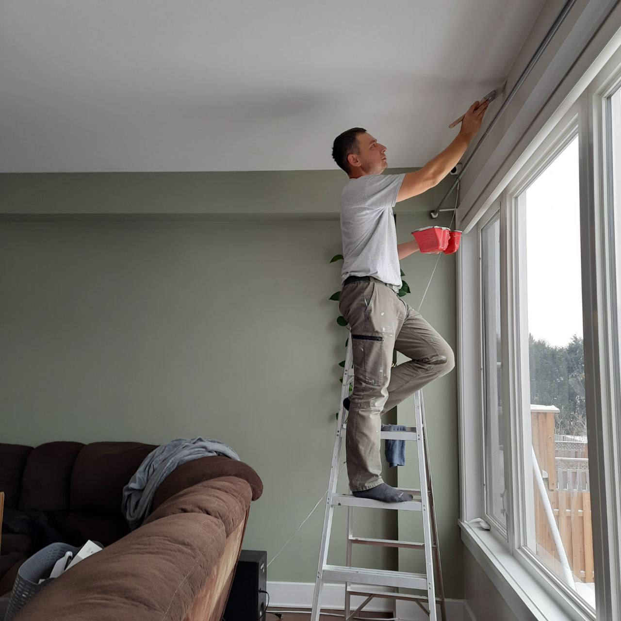 Painter cutting in a clean edge along a window frame from a step ladder in a living room